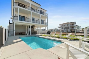 A multi-story building with a swimming pool, outdoor seating, and a gated entrance. - The Grand View by Brunswick Vacation Rentals: New 5BR Home w/ Elevator & Pool (Ocean Isle Beach)