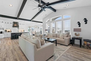 A spacious living area with a sofa, coffee table, and a view of the kitchen. - The Grand View by Brunswick Vacation Rentals: New 5BR Home w/ Elevator & Pool (Ocean Isle Beach)