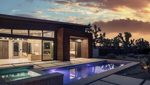 Ett modernt hus med en swimmingpool, stora fönster och en ökenliknande omgivning.