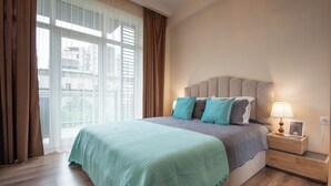 Una camera da letto con un letto grande, un comodino con una lampada e vista sui palazzi dalla finestra.