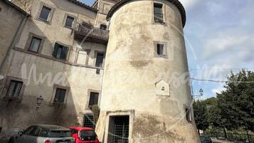 A historic building with a round tower, a cobblestone street, and parked cars.