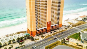Hotel alto com várias varandas, situado perto de uma praia com área de estacionamento e acesso rodoviário.