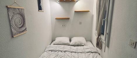 Un dormitorio pequeño y ordenado con una cama individual, estante en la pared y un cuadro enmarcado.