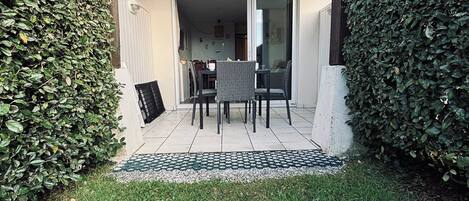 A patio area with a table and chairs, surrounded by hedges and a grassy lawn.