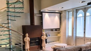 A modern living room with a glass staircase, a fireplace, a flat-screen TV, and a large window.