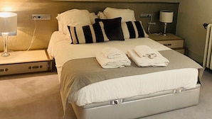 A neatly made bed with striped pillows, a bedside lamp, and a suitcase on the floor.