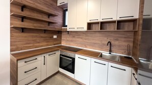 A modern kitchen with wooden shelves, white cabinets, and a stainless steel sink. - I&I Apartments III (Kragujevac)