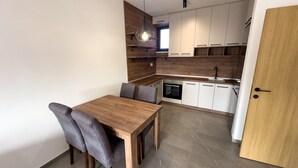 A compact kitchen with a wooden dining table and chairs, white cabinets, and a built-in oven. - I&I Apartments III (Kragujevac)
