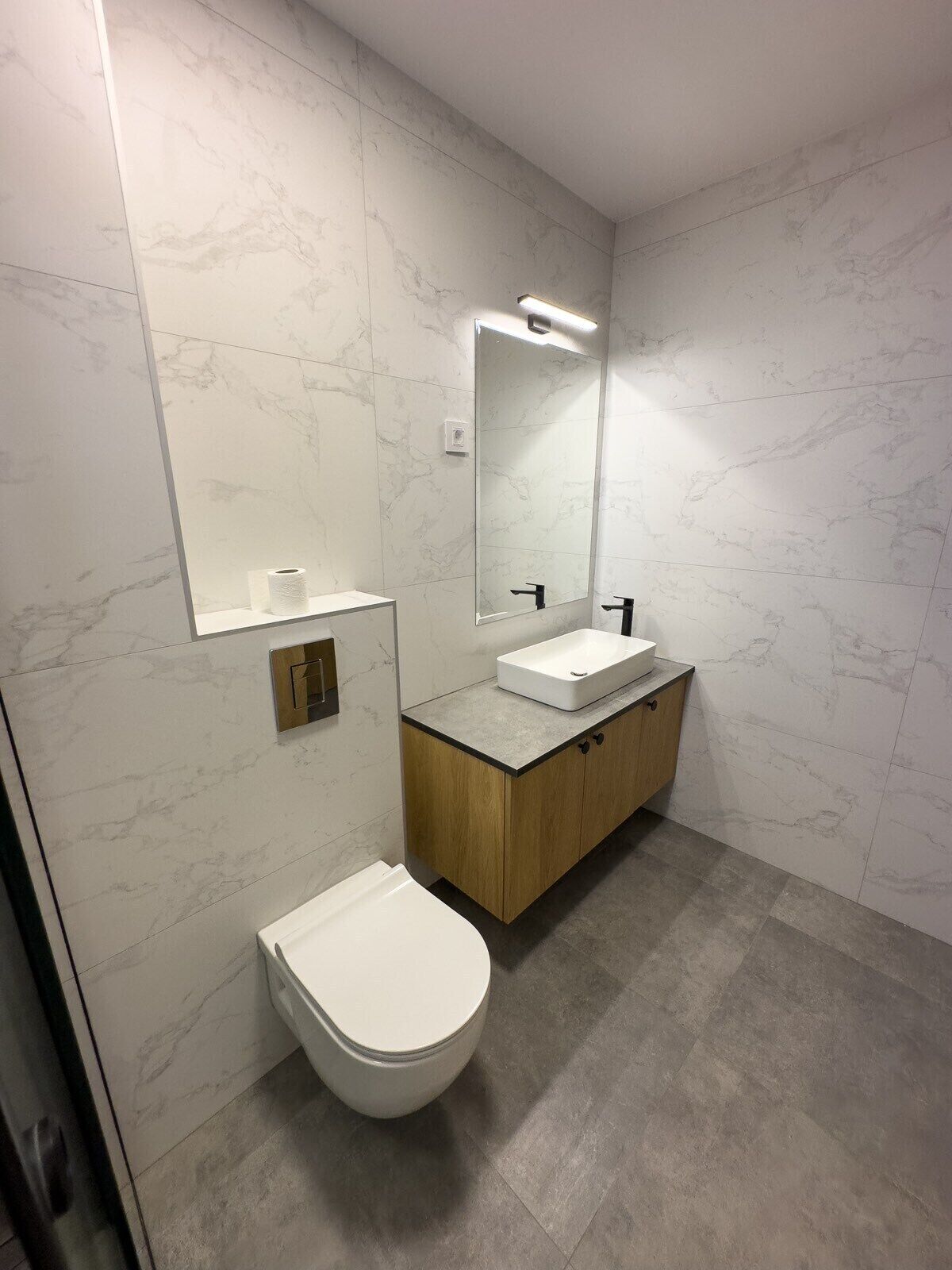 A modern bathroom with a white toilet, a sink with a mirror above it, and a wooden cabinet.