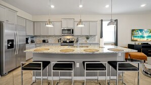 Une cuisine moderne dotée d’appareils électroménagers en acier inoxydable, d’un îlot en granit et de luminaires suspendus.