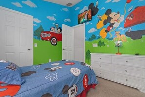 Ein Zimmer mit einem Bett, einem Schminktisch und einer Wand mit Zeichentrickfiguren.