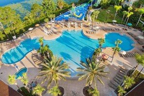 A large outdoor swimming pool with multiple sections, surrounded by palm trees and lounge chairs.