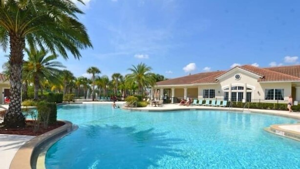 A large outdoor swimming pool surrounded by palm trees and a building with a tiled roof.