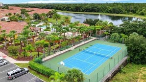 A tennis court surrounded by lush greenery and a body of water.