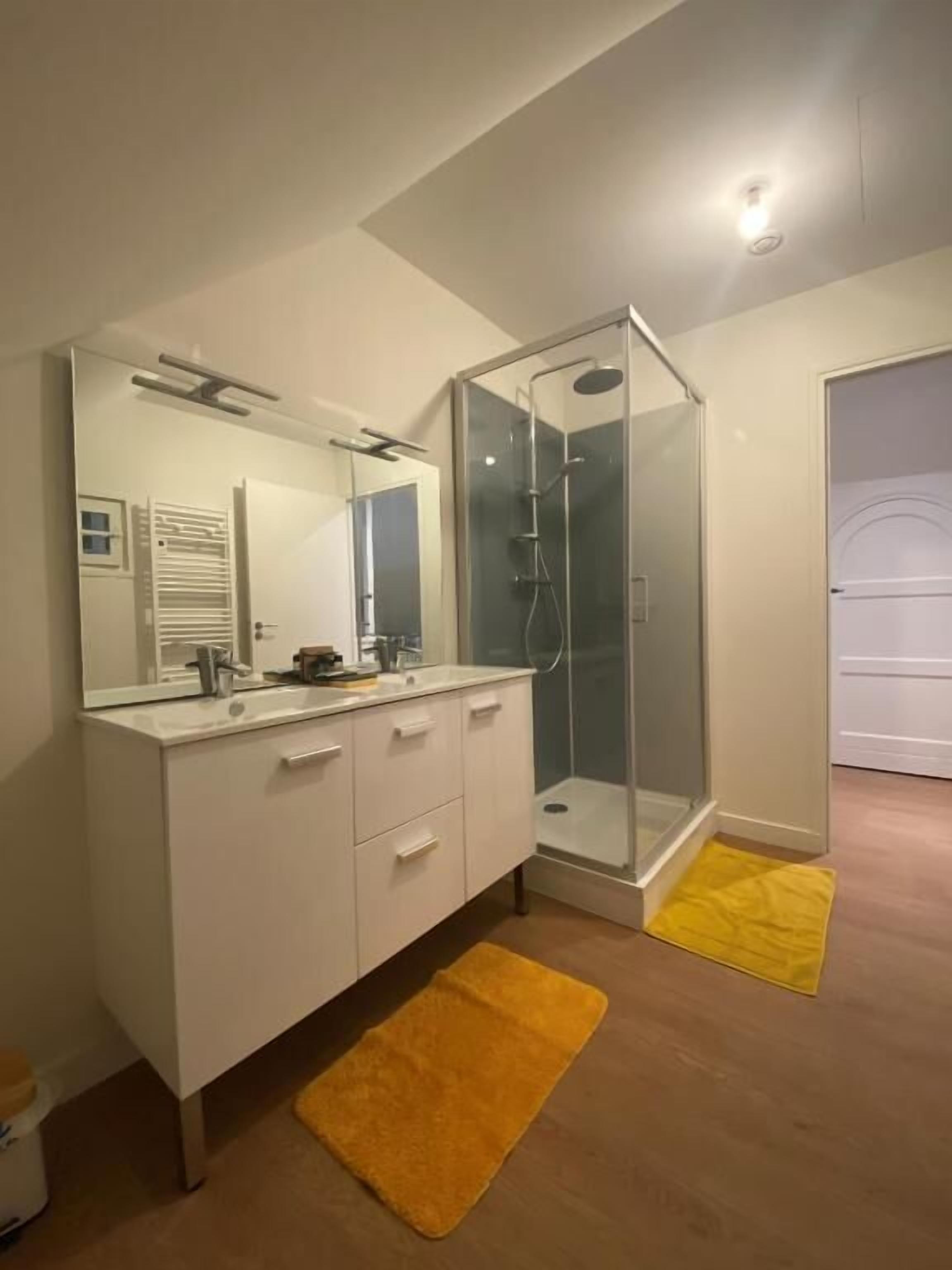 A modern bathroom with a glass shower enclosure, a white vanity, and a yellow bath mat.