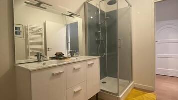 A modern bathroom with a glass shower enclosure, a white vanity, and a yellow bath mat.