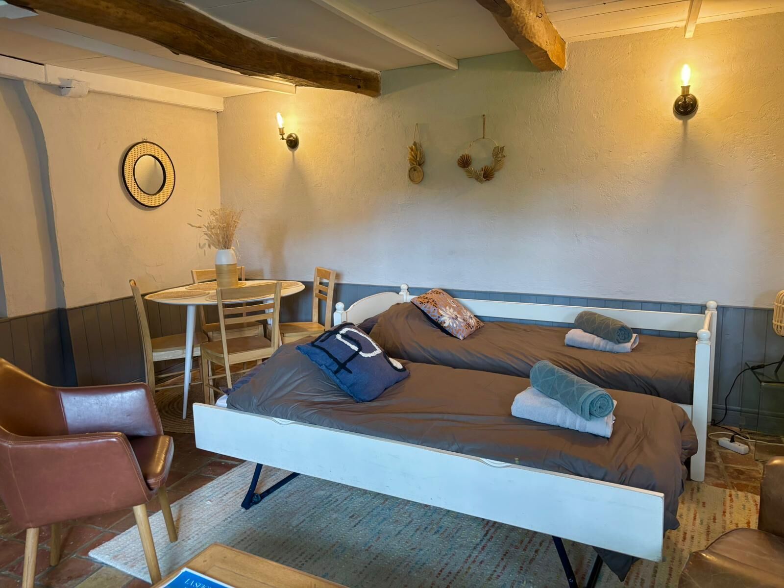A single bed with a headboard, a small round table with chairs, a wall-mounted lamp, and a wall clock.