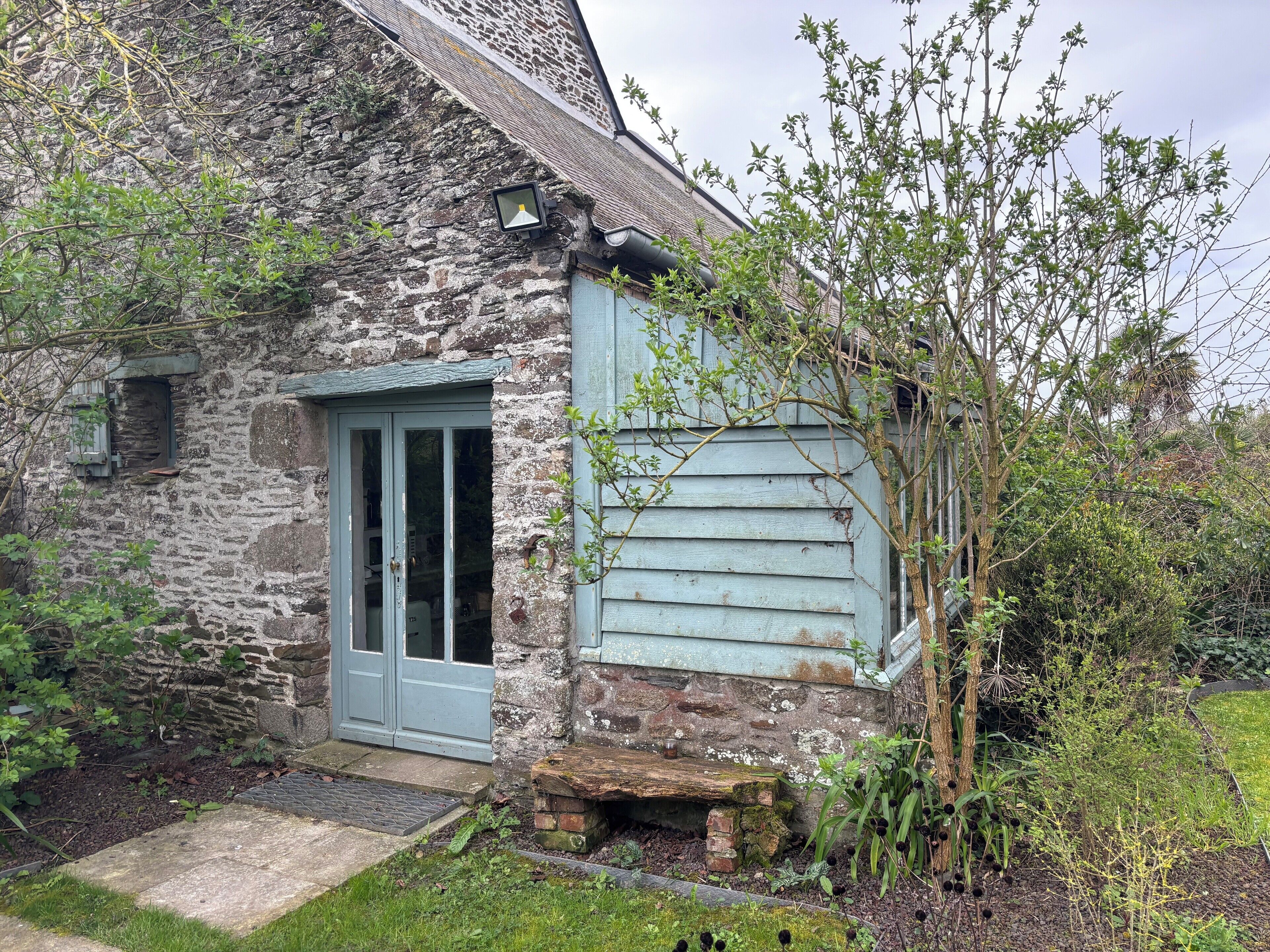 A stone building with a blue door, a small porch, and a garden area.