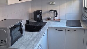 A compact kitchen with white cabinets, a built-in microwave, a coffee maker, and a kettle on the countertop. - Studio per week  (Menton)