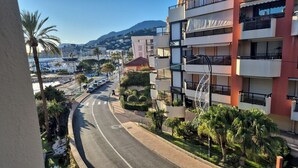 A multi-story building with balconies, a street with cars, and a mountain in the background. - Studio per week  (Menton)