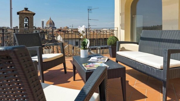 A terrace with wicker furniture, a potted plant, and a view of a historic building with a bell tower. - Luxurious 6-Bedroom Apartment in a Historic Palazzo with Panoramic Terrace





 (Firenze)