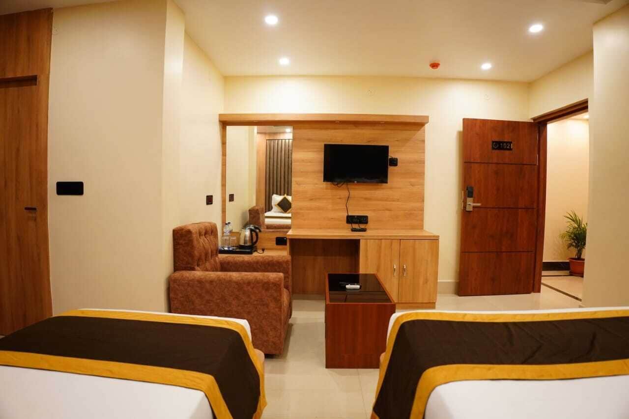 A hotel room with two beds, a TV mounted on the wall, a small table, a sofa, and a wooden cabinet.