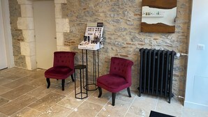 A lobby with stone walls, two red chairs, a standing display of toiletries, and a radiator. - Maison d'hôtes La Bellours (Cahors)