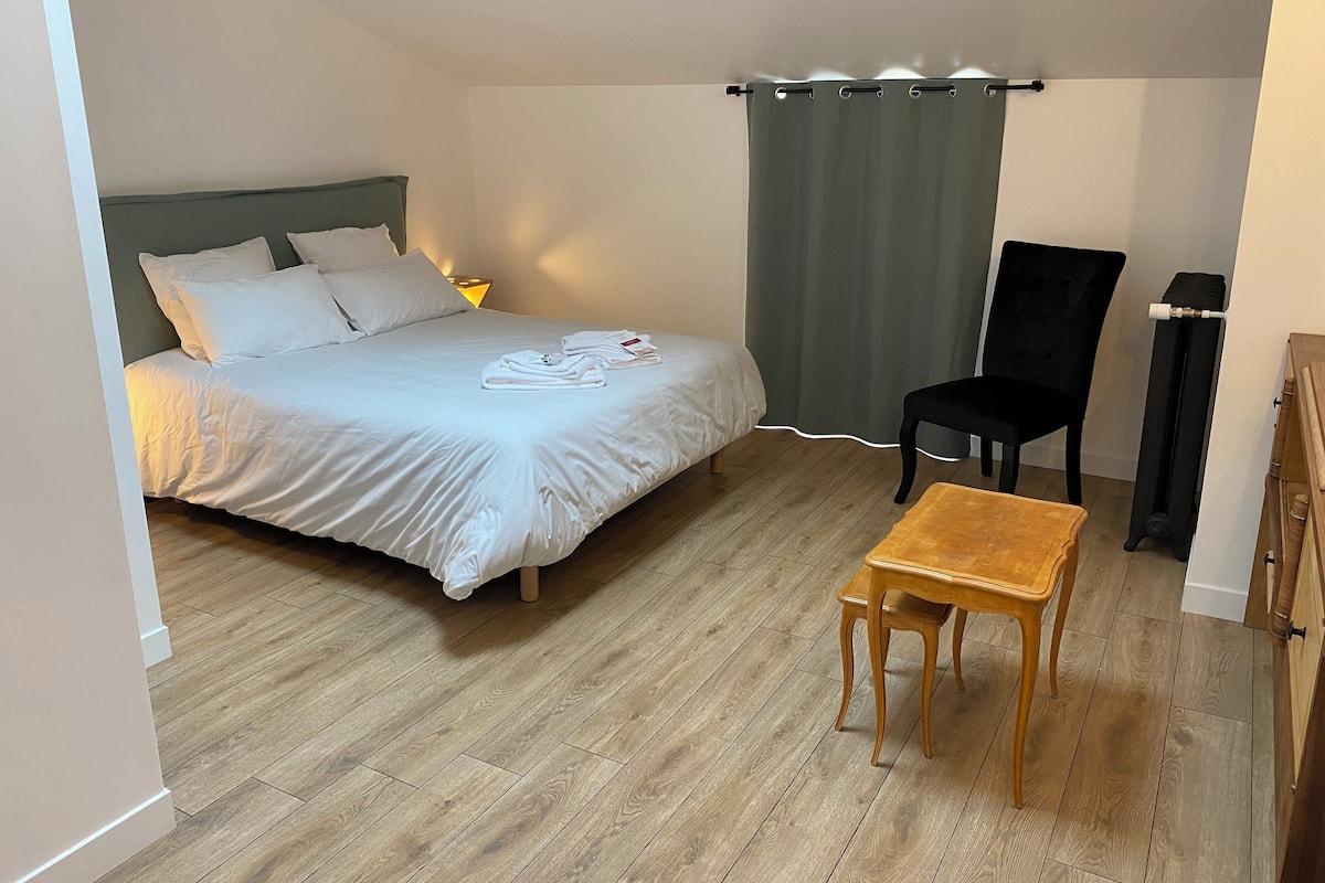 A bedroom with a bed, a chair, a small table, and a curtain.