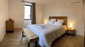 A neatly made bed with white linens, a bedside table with a lamp, a wooden bench, and a small cabinet. - Maison d'hôtes La Bellours (Cahors)