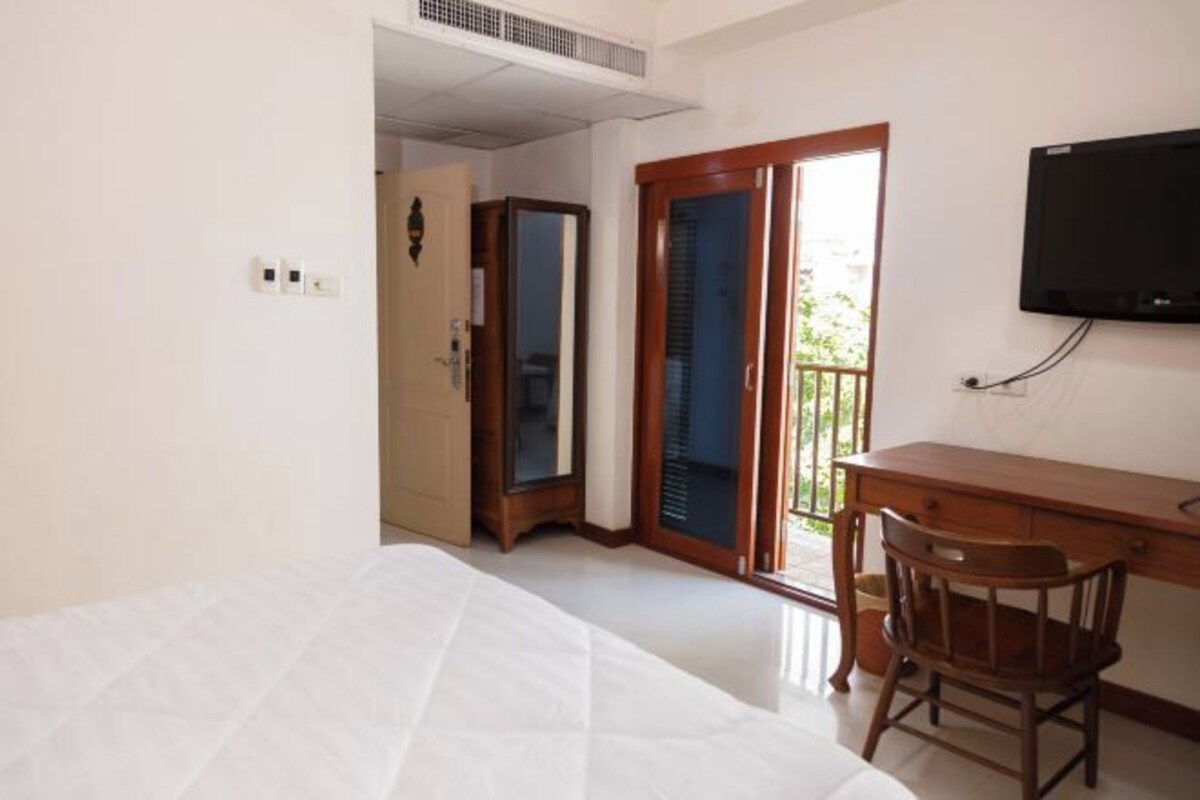 Habitación de hotel con cama, escritorio con silla, televisor y puerta corrediza de vidrio que da a un espacio exterior.