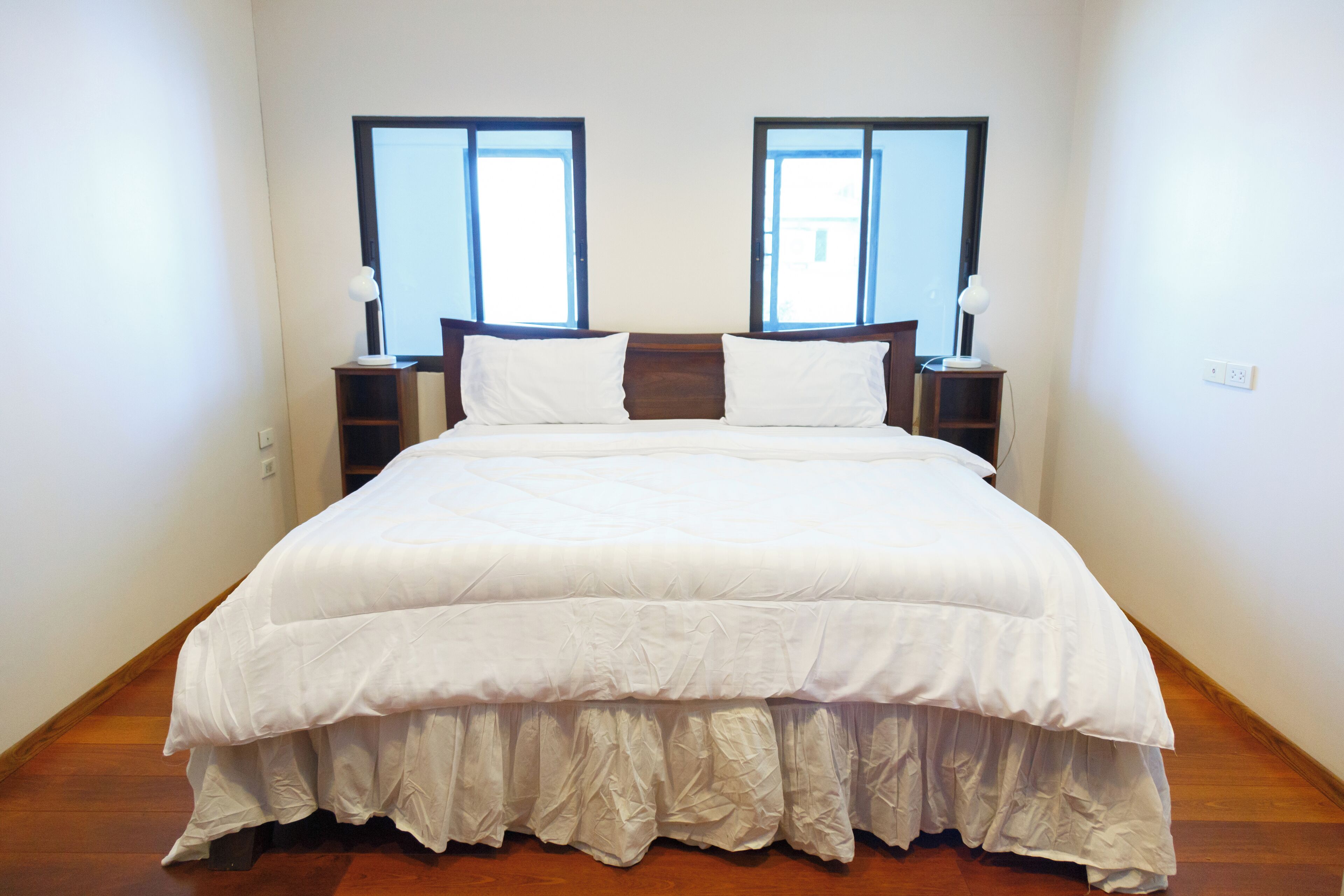 A neatly made bed with white bedding, two bedside tables with lamps, and a window with a view.