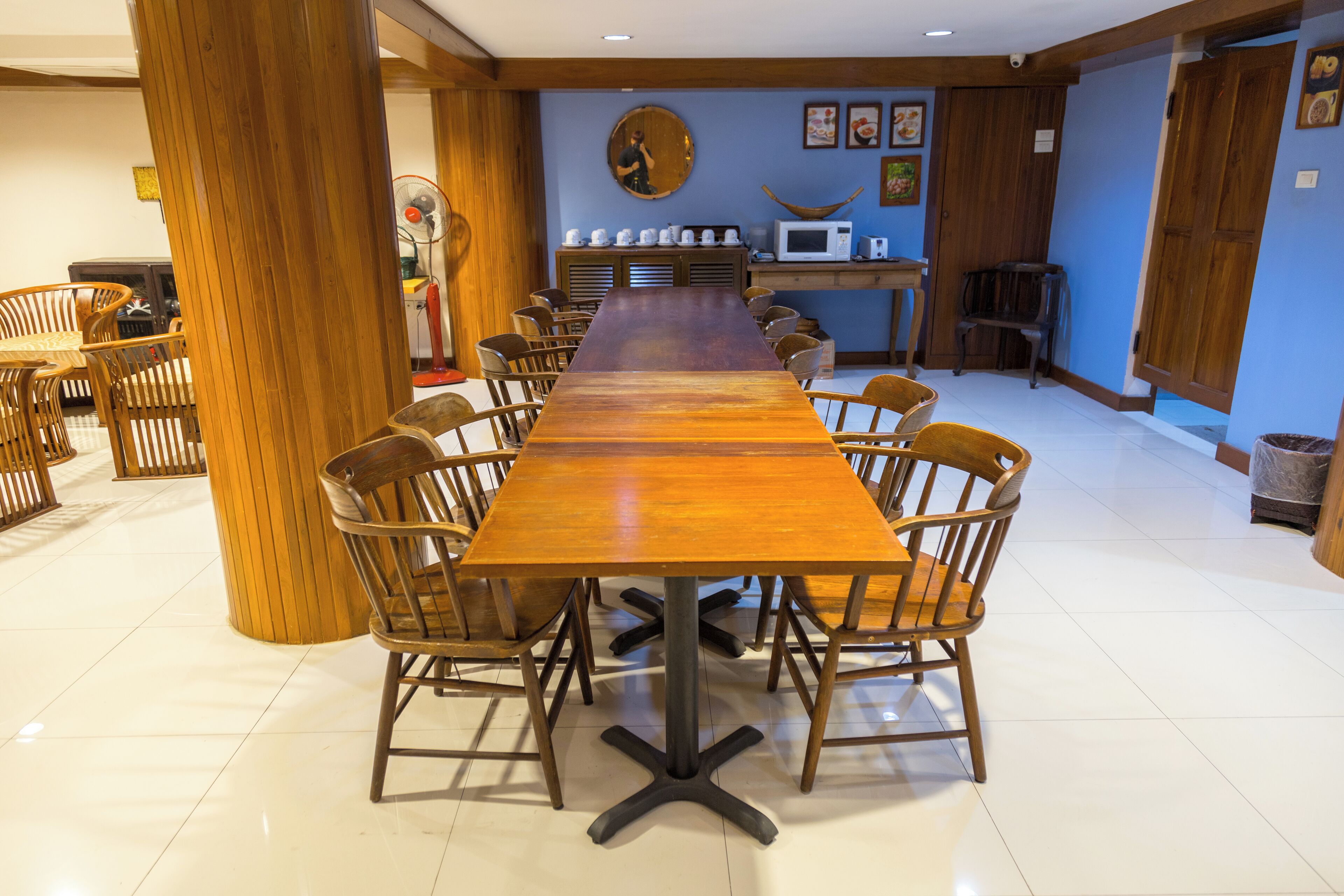Un grand espace dédié à la salle à manger, avec une longue table en bois entourée de chaises, un four à micro-ondes et un ventilateur.