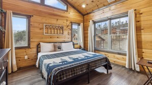 Een slaapkamer in een houten hutje, met een bed, nachtkastje en raam met gordijnen.