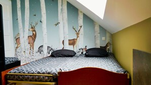 Een slaapkamer met een schuine plafond, een bed met een beddengoed met een patroon, en een muurschildering van herten en vogels.