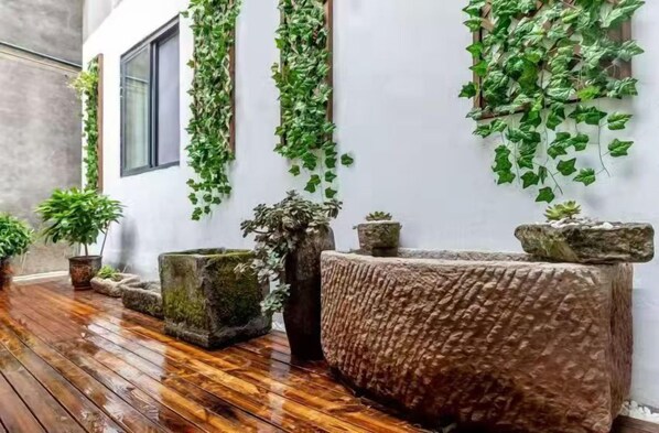 A wet wooden floor, a stone bench, and green plants growing on walls. - Panda House Hotel (Chengdu)