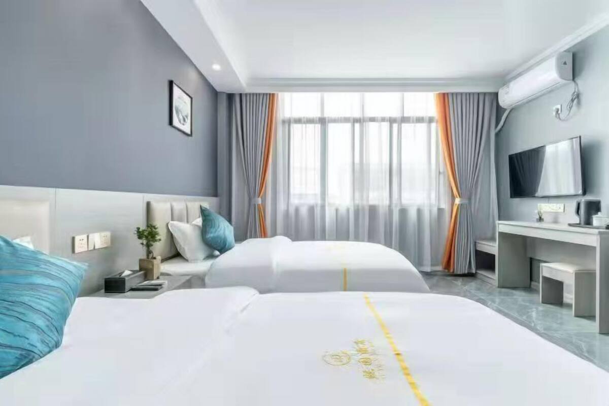 A hotel room with two beds, a desk, a TV, and a large window with curtains.