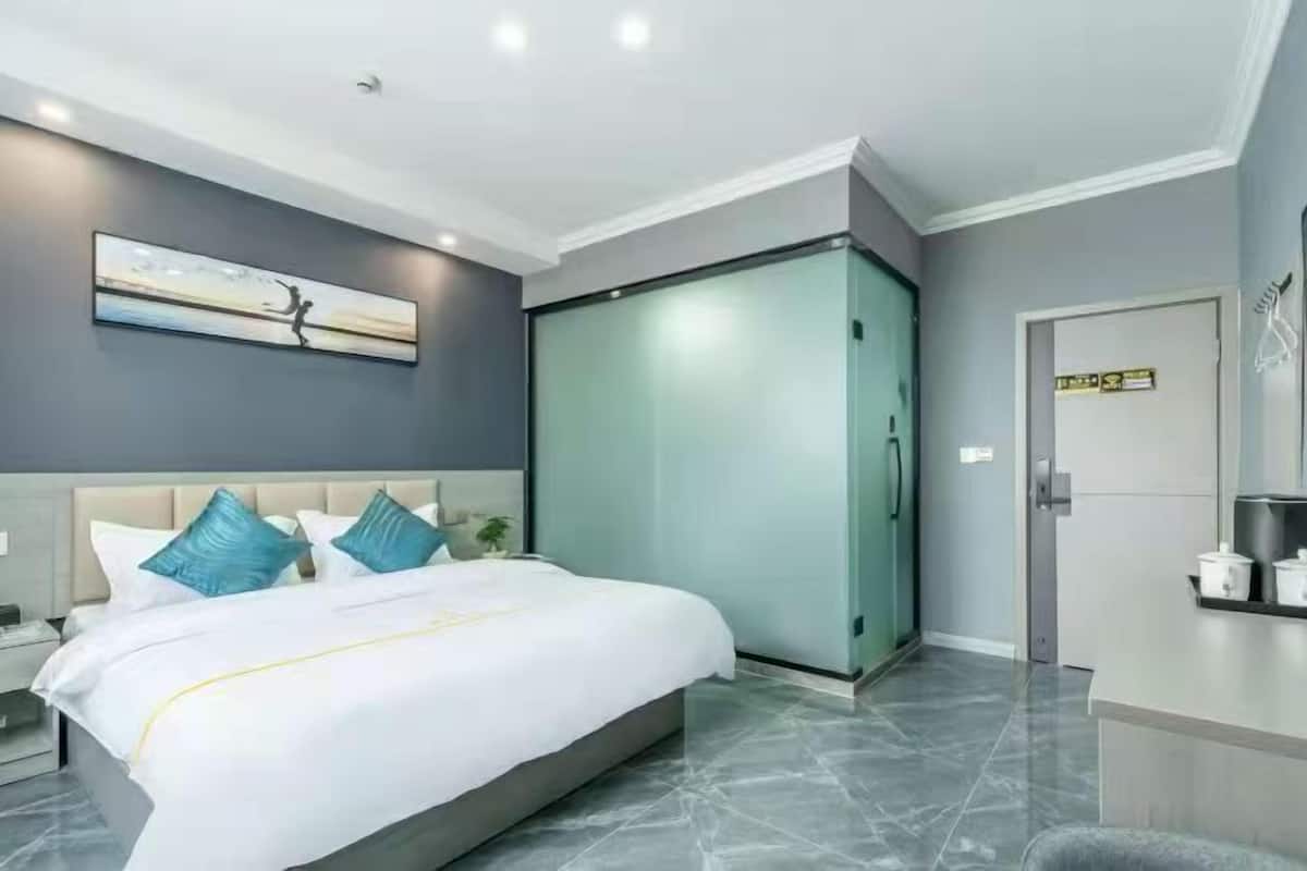 A modern hotel room with a large bed, a nightstand, a wardrobe, and a painting on the wall.