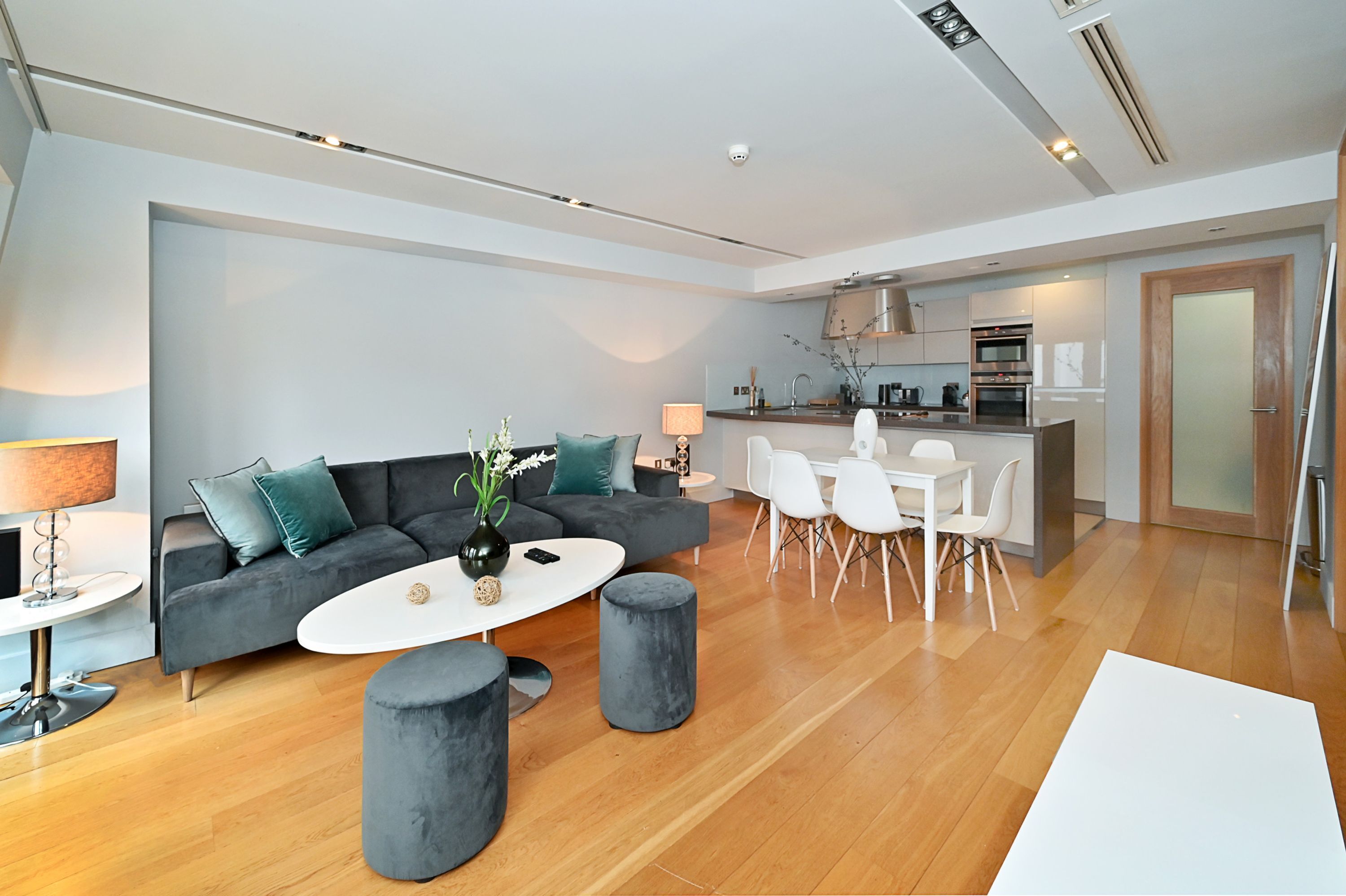 A modern living room with a grey sofa, a round coffee table, and a dining area with white chairs.