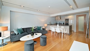 Un salon moderne avec un canapé gris, une table basse ronde et un coin repas avec des chaises blanches.