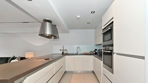 Une cuisine moderne avec des meubles blancs, un four en acier inoxydable et un îlot central surmonté d’un luminaire.