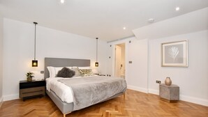 Een moderne slaapkamer met een groot bed, nachtkastjes, een nachtkastje, een potplant en een kunstwerk in een lijst aan de muur.