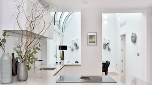 Een modern interieur met een minimalistisch ontwerp, met een keukenhoek, een strak aanrecht, een ingebouwde kookplaat en een grote spiegel die de ruimte weerspiegelt.