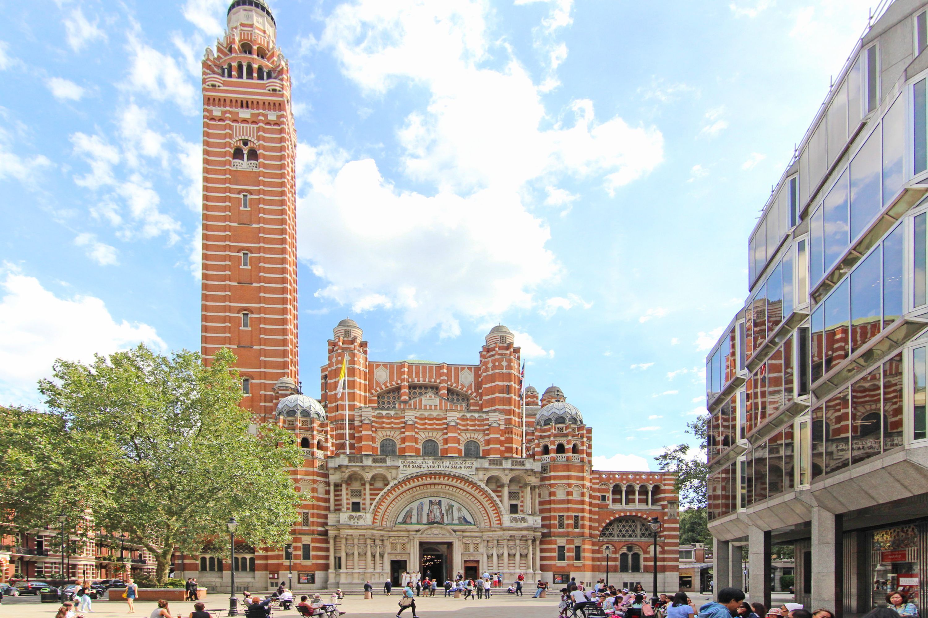 A historic building with a prominent tower and arched windows, surrounded by modern structures.