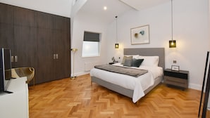 Een moderne slaapkamer met een groot bed, houten vloeren, een kledingkast en hanglampen.