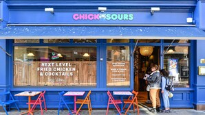 Une devanture bleue avec une enseigne indiquant « CHICK IN SOURS » et un menu proposant des plats comme du poulet frit et des cocktails.