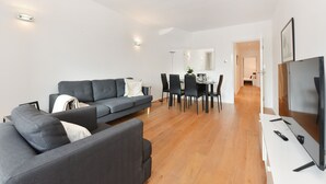 A modern living room with a grey sofa, dining table, chairs, and a flat-screen TV. - Cromwell Style II - 353pw (London)