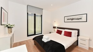 A modern hotel room with a large bed, a bedside table, a nightstand, a window with blinds, and a framed picture on the wall. - Cromwell Style II - 353pw (London)