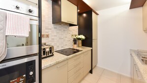 A modern kitchen with a built-in oven, a toaster, a black refrigerator, and a countertop with a vase of flowers. - Cromwell Style II - 353pw (London)