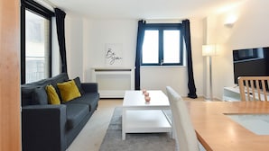 Una sala moderna con un sofá gris, una mesa de centro blanca, una mesa de comedor de madera y un televisor.