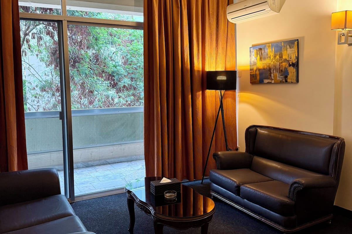 A hotel room with a large sliding glass door, a black leather sofa, a small table with a tissue box, and a painting on the wall.